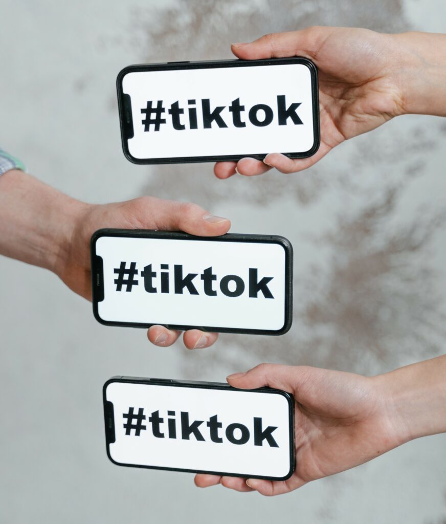Three different hands, each holding a mobile device with #tiktok on the screen, symbolizing the social and communal nature of the service.