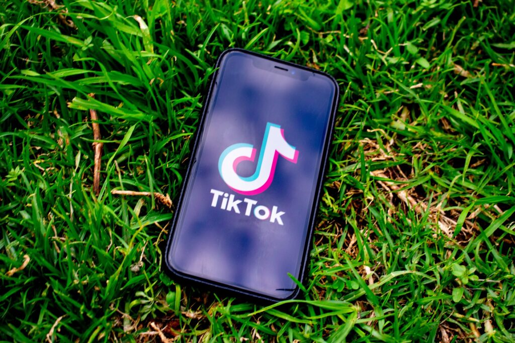 A mobile device with TikTok on its screen, laying in a lush green lawn symbolizing the new, fresh, evergreen nature of the service.